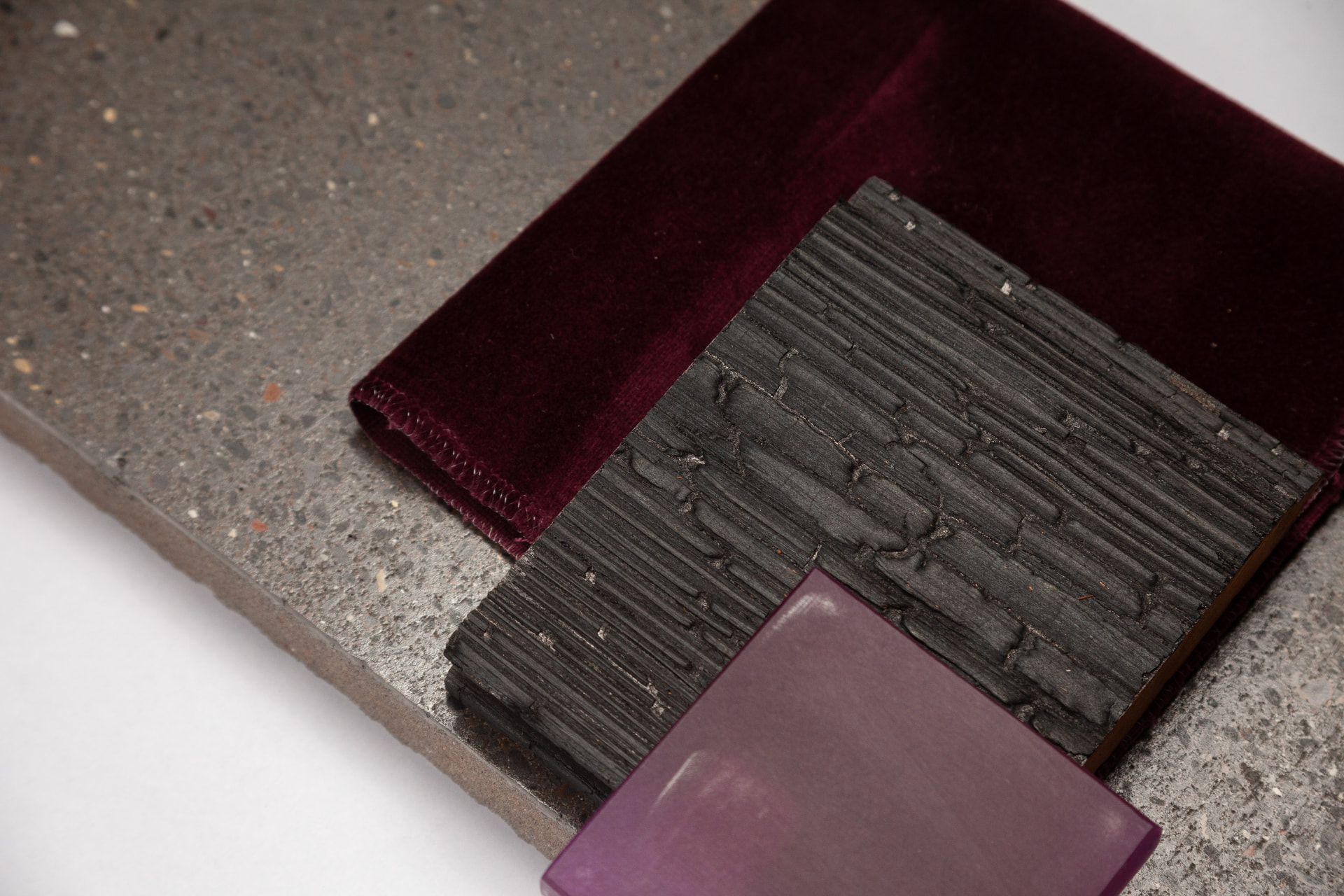 Burgundy velvet, charred timber and violet resin samples on concrete
